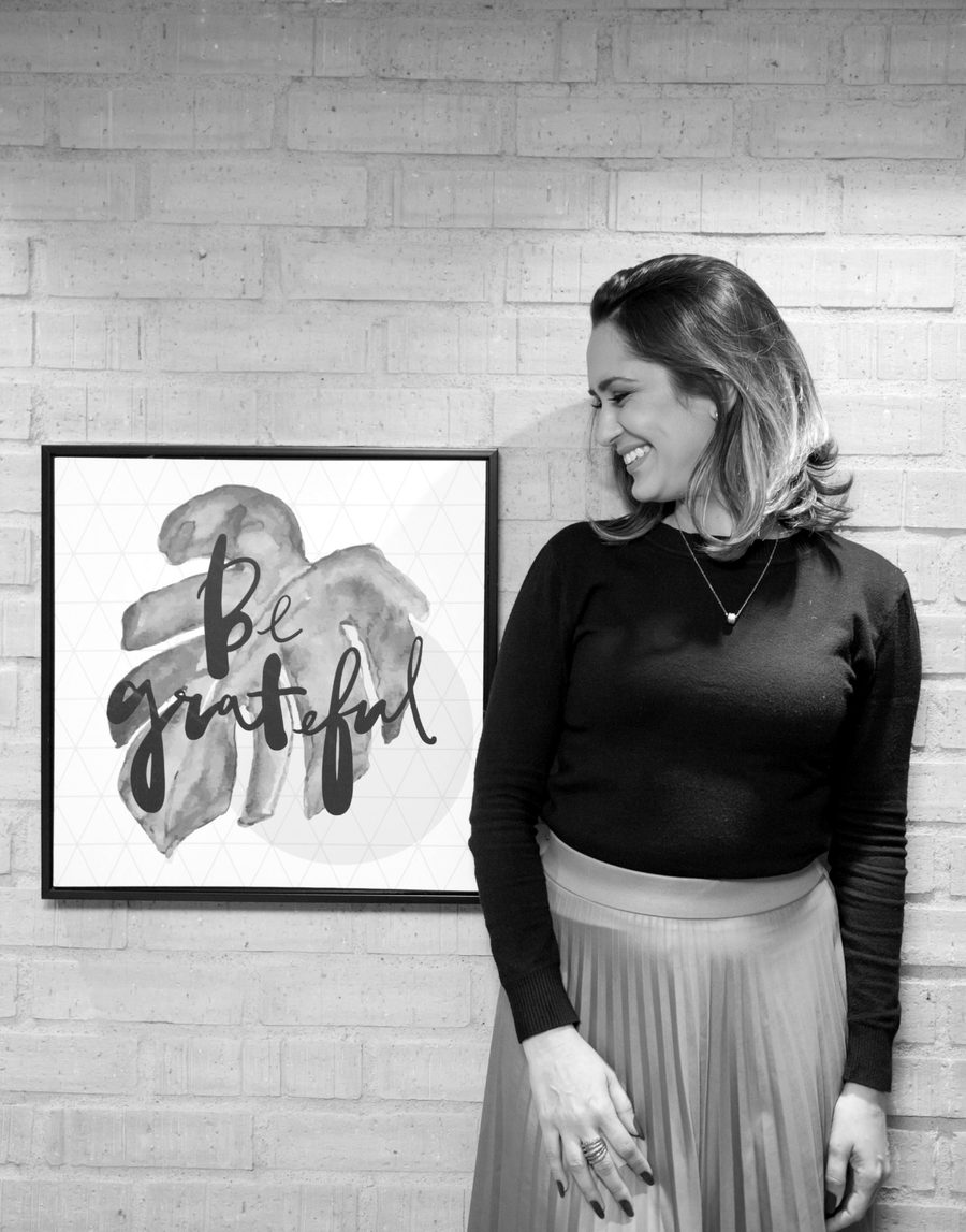 Andressa Costa sorrindo em frente a uma parede de tijolos, ao lado de um quadro